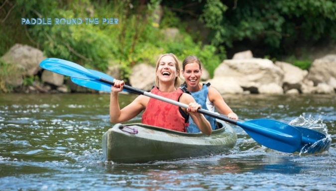 Two women kayaking during pregnancy, smiling and paddling on a serene river.