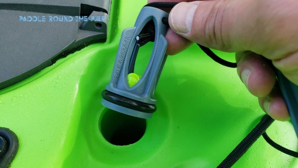 Close-up of a hand holding kayak scupper plugs above a hole in a green kayak