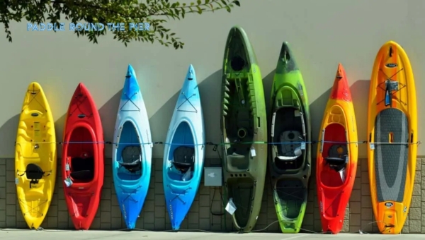 A row of colorful kayaks, varying in size and kayak weight, lined up against a wall.